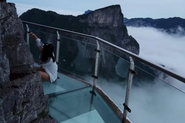 Tourist sitting on a glass walkway on a cliff edge